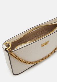Crèmekleurige handtas met een textuurovervlak, voorzien van een gouden kettingriem, ritssluiting en een logo aan de voorkant. Het interieur heeft meerdere vakken.