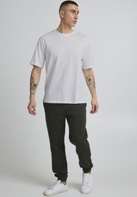 Witte katoenen t-shirt met korte mouwen, gecombineerd met donkergroene joggingsbroek en witte sneakers. Eenvoudig ontwerp, relaxte pasvorm.