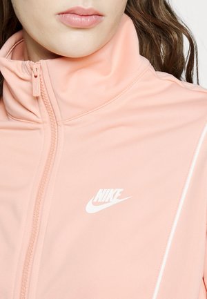 Close-up of a person wearing a light pink Nike jacket with a zip-up collar and white logo on the chest.