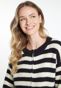 Strickjacke mit schwarz-weißen vertikalen Streifen, einem runden Ausschnitt und einem Reißverschluss auf der Vorderseite. Glatte Textur und gerippte Bündchen.