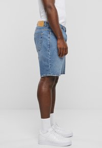 Shorts en denim de lavage bleu clair, en tissu coton, coupe droite, longueur genou, avec ourlet cousu et poches arrière. Portés avec des baskets blanches.