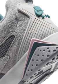 Gros plan sur une chaussure de sport en suède gris et mesh avec un design perforé, des accents bleu sarcelle et rose, et une semelle texturée.