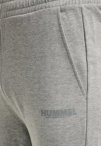 Primer plano de pantalones deportivos gris claro con bolsillo lateral y logo "HUMMEL" impreso cerca de la costura del bolsillo.