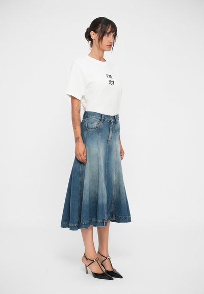 Fustă din denim în degradé de la albastru deschis la albastru închis, asociată cu un tricou alb cu text negru și pantofi negri cu vârful ascuțit.