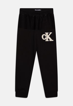 Pantalon de jogging noir avec taille élastique et cordon, avec logo blanc « cK » sur la partie supérieure de la cuisse gauche, poignets côtelés aux chevilles.