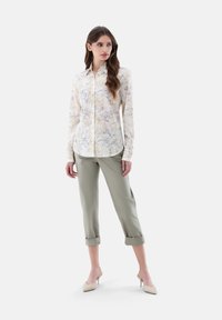 Camicia floreale a maniche lunghe gialla e grigia, abbinata a pantaloni leggeri verde chiaro con risvolto. Il modello indossa scarpe con tacco beige.