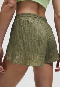Närbild av en person som bär texturerade olivgröna träningsshorts med elastisk midja och en limegrön sportbehå.