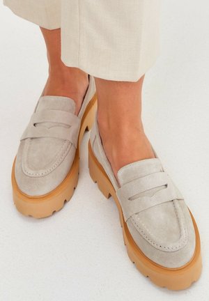 Mocassins en daim gris clair avec une semelle épaisse et robuste de couleur beige. Présentent un design classique de mocassin avec des détails de couture légers sur la tige.