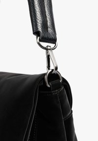 Esquina de un bolso de cuero negro con una correa texturizada y un clip de metal. Presenta un acabado suave y liso, y un diseño estructurado sutil.