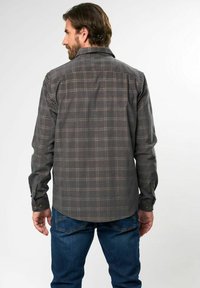 Camisa de cuadros gris de manga larga con cuello abotonado, con detalles en azul y rojo, hecha de una tela texturizada, metida dentro de unos jeans azules.