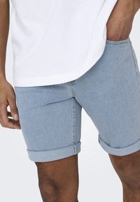 Vaaleansinisiä farkkushortseja, joissa on käännetyt lahkeet, klassinen muotoilu ja slim fit. T-paidan alaosat näkyvät osittain ylhäältä.