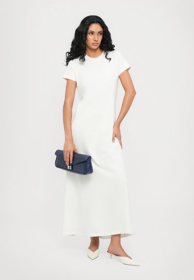 Abito lungo bianco a maniche corte in un tessuto morbido, abbinato a una pochette blu navy, tacchi beige a punta e un'acconciatura elegante.