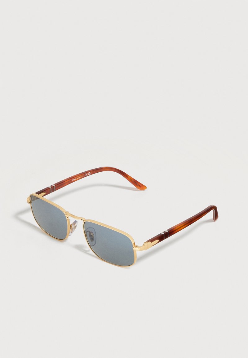 Ορθογώνια γυαλιά ηλίου με χρυσό μεταλλικό σκελετό, φακούς με μπλε απόχρωση και καφέ βραχίονες με σχέδιο χελώνας σε λευκό φόντο.