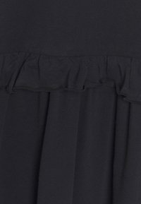 Svart klädestyg med en volangkant. Materialet verkar slätt med en lätt lyster. Vertikal drapering förbättrar textur och flöde.