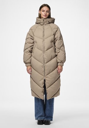 Cappotto lungo beige in piuma con design a losanga, colletto alto e chiusura con zip; indossato sopra pantaloni di jeans a gamba larga blu.