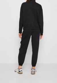 Svart sweatshirt med hög krage och ribbad nederkant, tillsammans med matchande joggers med vita sidostripes och elastiska manschetter.