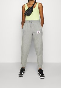 Lichtgroen tanktop met kantafwerking, grijze trainingsbroek met elastische manchetten en logo-opdruk, compleet met zwarte sneakers en een kleine zwarte schoudertas.