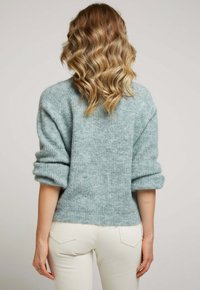 Pull en tricot doux bleu clair avec une finition texturée, épaules tombantes et poignets retroussés. Présente un design court et un ourlet côtelé.