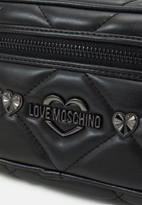 Svart kviltad faux läderhandväska med metallblixtlås, präglad "Love Moschino"-logotyp och hjärtformade accentdetaljer.