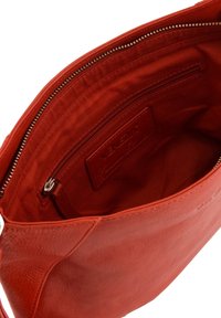 Sac à main en cuir rouge avec une surface texturée, fermeture éclair et poche intérieure. Il dispose d'un revêtement lisse et d'une étiquette de marque.