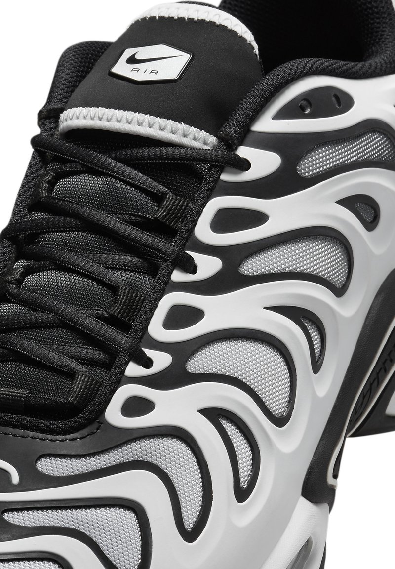 Chaussure de sport en noir et blanc avec une tige en maille ornée de motifs fluides et ondulés, lacets noirs et logo Nike Air argenté sur la languette.