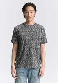 Camiseta gris y negra con moteado, de mangas cortas, cuello redondo y textura suave. Combinada con jeans de color azul claro.