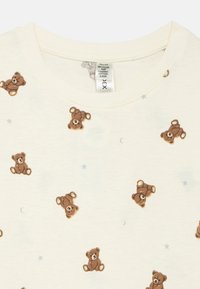 Maglietta crema chiaro a maniche corte realizzata in una miscela di cotone riciclato e biologico, con un motivo di orsacchiotti marroni e piccole stelle blu.