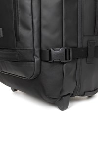 Black wheeled duffel bag made of durable fabric, featuring a side mesh pocket, sturdy buckle clasp, and textured body for grip.