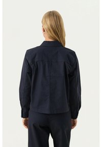 Granatowa kurtka z długimi rękawami, kołnierzem i prostym krojem. Posiada widoczne szwy i gładką fakturę.