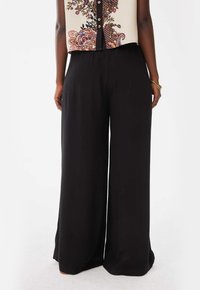 Zwarte wijde broek van gladde stof, met een elastische tailleband, die zorgt voor een ontspannen pasvorm en volledige dekking.