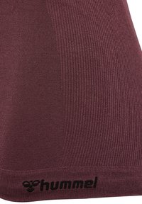 Nahaufnahme von weinrotem, geripptem Stoff mit unten am Rand in Schwarz besticktem "hummel"-Logo.