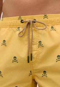 Șorturi de baie galbene cu un cordon la talie, decorate cu un model de craniu și oase încrucișate verzi, realizate dintr-un material ușor și neted.