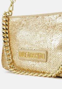Goldene Pailletten-Clutch mit dickem goldenen Kettenriemen und "LOVE MOSCHINO" Logo-Plakette auf der Vorderseite vor weißem Hintergrund.