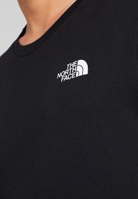 Primer plano de una camiseta negra con el logotipo blanco de "The North Face" en la parte superior del pecho, cerca del escote.