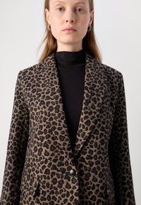 Leopardenmuster-Blazer in Braun und Schwarz, mit spitzem Revers, einer Knopfverschluss und zwei vorderen Taschen. Glatte Stoffstruktur.