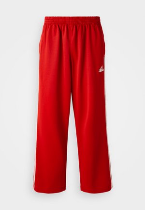 Raudoni sportiniai kelnės su elastingu juosmeniu, su baltais šonais ir maža prekinio ženklo logotipu kairėje klubo pusėje. Pagamintos iš lengvos medžiagos.