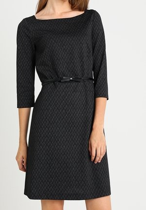Sort knælængde kjole med subtilt diamantmønster, trekvartærmer, bådudskæring og tyndt sort bælte med sløjfe i taljen.