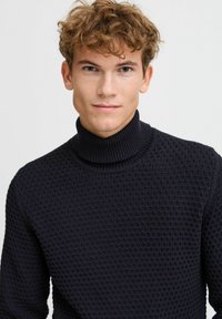 Maglione a collo alto di colore navy con motivo a maglia testurizzato, colletto e polsini a costine, design aderente. Colore scuro uniforme senza ulteriori accenti.