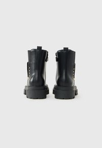Schwarze Leder-Ankle-Boots mit einer klobigen schwarzen Sohle, seitlichen elastischen Einsätzen und goldenen Nietenakzenten auf den Außenseiten.