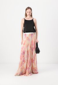 Schwarzsatin-Camisole, plissierter langer Rock im pastellfarbenen Blumenmuster, strukturstoff und eine kleine schwarze Handtasche in geometrischer Form.