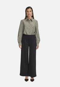 Blusa de rayas verdes con bordado floral, frente con botones; combinada con pantalones negros de pierna ancha y talle alto y zapatos planos marrones.