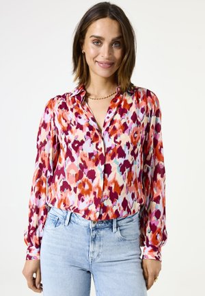Blusa de seda de manga larga con un estampado animal vibrante en rosa, rojo y púrpura; presenta botones en la parte delantera y un cuello clásico.