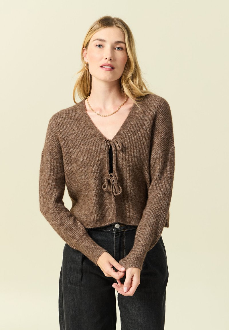 Maglione corto in maglia marrone con scollo a V, chiusura con nodo davanti e maniche lunghe. Tessuto strutturato e polsini a coste.