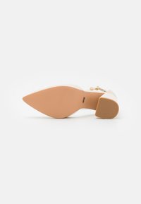 Korkokenkä, jossa on terävä kärki ja sileä synteettinen päällinen, beige väri. Pohja on vaaleanruskea, jossa on rakenteellinen pinta pidon parantamiseksi.