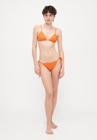 Oranž da bathing set, mis sisaldab ribat kangast, kolmnurkset ülemist osa ja reguleeritavaid sidumisäärtega põhjasid. Lihtne disain, millel on minimaalne riistvara.
