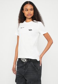 Λευκό T-shirt με κοντά μανίκια που διαθέτει γραφικό σχέδιο ματιού στο μπροστινό μέρος. Συνδυάζεται με σκουρόχρωμο παντελόνι cargo και μαύρη ζώνη με ασημένια αγκράφα.