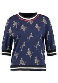 Marinblus med korta ärmar som har ett leopardmönster. Den har en rund halsringning med kontrasterande röda och vita ränder, samt randiga manschetter.