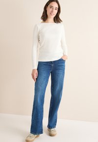 Witte geribde longsleeve top gecombineerd met blauwe denim brede pijpen jeans. De jeans hebben een klassiek vijf-pocket ontwerp en lichte slijtage.