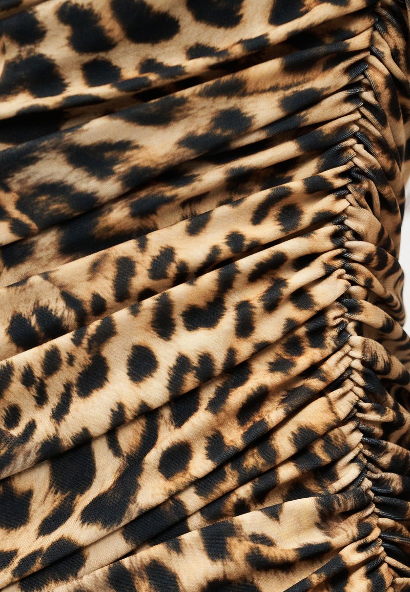 Tissu à imprimé léopard avec une texture froncée, présentant un mélange de motifs beige et noirs, une surface lisse et des détails froncés le long des coutures.