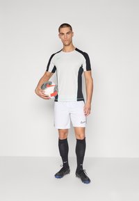 Nike urheiluvaatteet, joissa harmaa ja musta lyhythihainen paita, valkoiset shortsit, mustat polvisukat ja kuvioitu jalkapallo.